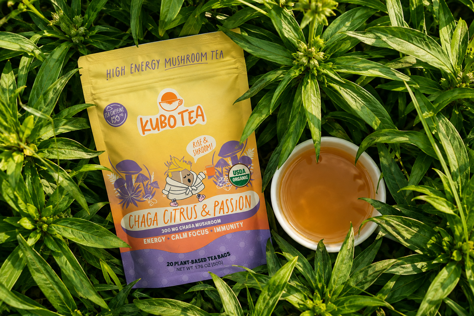 A stand-up pouch of Kubo Tea Ghaga Citrus & Passion high energy mushroom tea lies on a bed of green leaves next to a small white cup filled with amber tea.